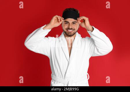 Happy young man in bathrobe and eye sleeping mask on red background Stock Photo