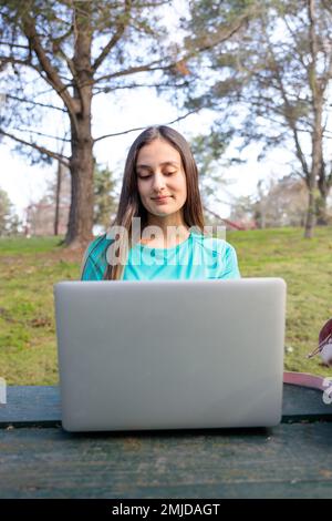 Young woman using a laptop and sitting outside in a park. Stock Photo