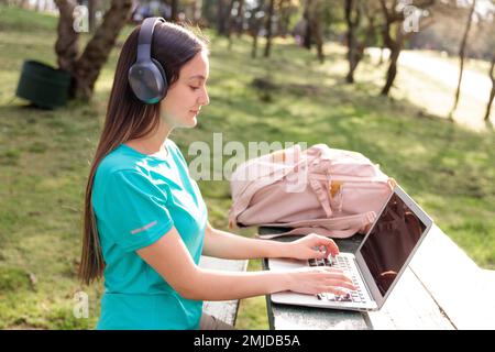 Female university student, sitting and using a laptop outside in a park Stock Photo