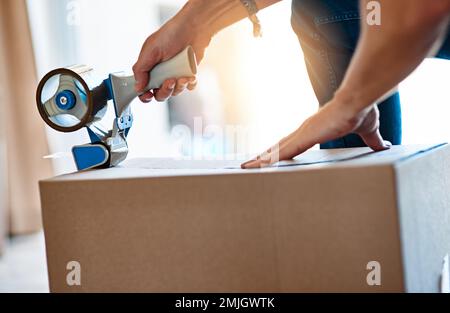 Wrap it, pack it, tape it. an unrecognizable young man closing a cardboard box with tape at home. Stock Photo