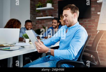 Creating another cutting edge design. a young designer working on a digital tablet with his colleagues in the background. Stock Photo