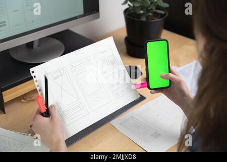 Sketch of wireframe for website. Women designer working on a mobile application, holding in hand phone with green screen Stock Photo