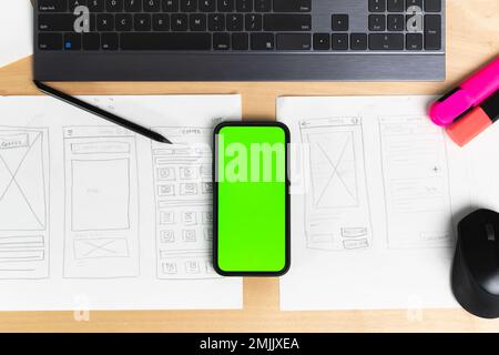 Sketch of wireframe for website. Women designer working on a mobile application, holding in hand phone with green screen Stock Photo