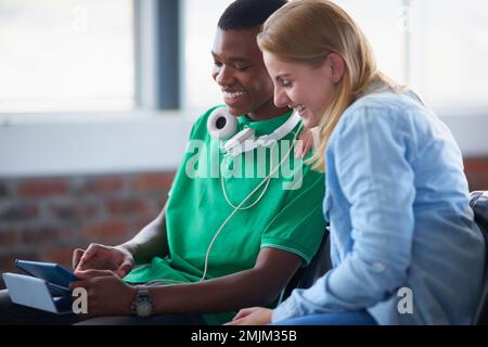 Lemme show you...two university students looking at a digital tablet while sitting in their classroom. Stock Photo