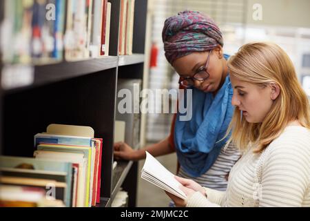 Thorough preparation is the key to better grades. two university students working together in the campus library. Stock Photo