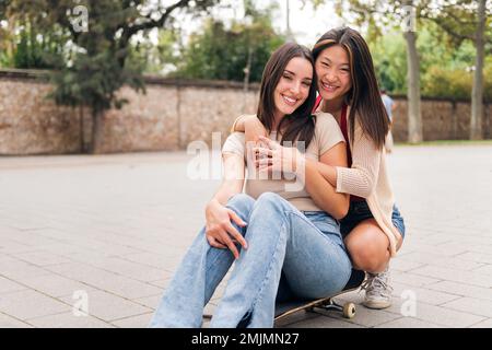 young couple of women sitting on a skateboard Stock Photo