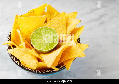 Nachos tortilla chips in a bowl. Bowl of corn tortilla chips and lime on concrete. Top view. Copy space Stock Photo