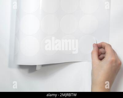a neat female hand peels off the round white sticker of the plotter trimming. mockup stickers Stock Photo