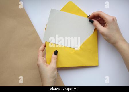 female hands with manicure holding a white sheet and a yellow envelope on a brown and white background. postcard layout Stock Photo
