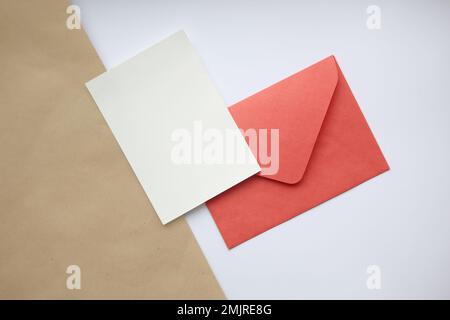 Postcard mockup vertical, on white and brown background red closed envelope and white sheet Stock Photo