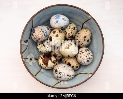 top view of many boiled quail eggs in ceramic bowl on light brown wooden table Stock Photo