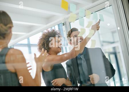 Success is having the best team behind you. coworkers using sticky notes against the wall during a brainstorming session. Stock Photo
