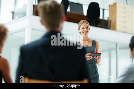 Another successful presentation in the books. a businesswoman holding a digital tablet while giving a presentation to colleagues in a modern office. Stock Photo