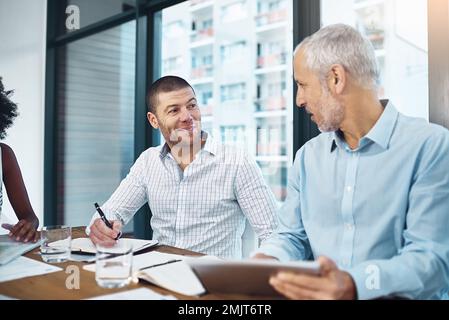Talking strategy in the boardroom. a group of coworkers talking together over a digital tablet in a meeting in an office. Stock Photo