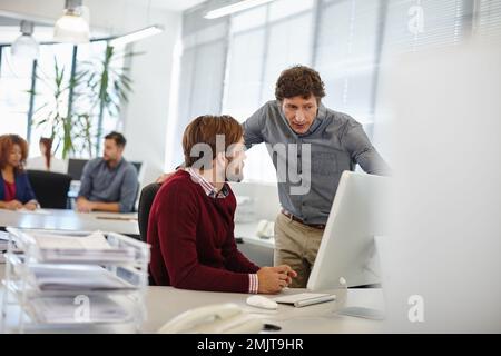 He takes his colleagues training seriously. a businessman and his colleague working together on a computer in the office. Stock Photo