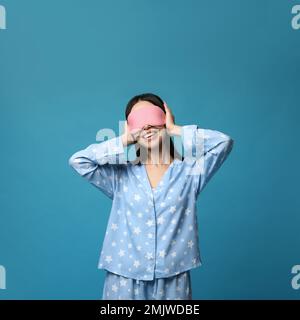 Young woman wearing pajamas and sleeping mask on blue background. Bedtime Stock Photo