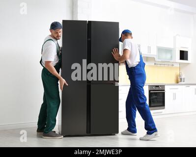 Professional workers carrying modern refrigerator in kitchen Stock Photo