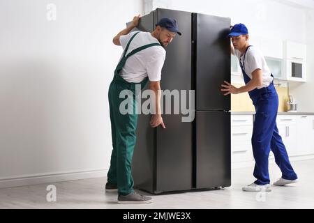Professional workers carrying modern refrigerator in kitchen Stock Photo