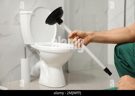 Professional plumber holding plunger near toilet bowl in bathroom, closeup Stock Photo