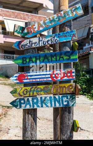 Ksamil, Albania - September 13, 2021: Street wooden sign arrows indicating directions to different places of the world in Ksamil riviera. Vacation con Stock Photo