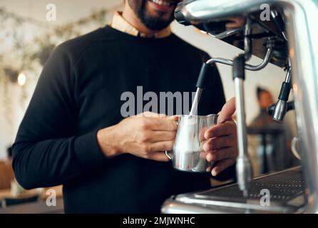 Hands, barista and brewing coffee in kitchen using machine for hot beverage, caffeine or steam. Hand of employee male steaming milk in metal jug for Stock Photo