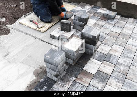 Worker laying gray paving slabs over cement base. Street paving works in progress. Background photo with selective focus Stock Photo