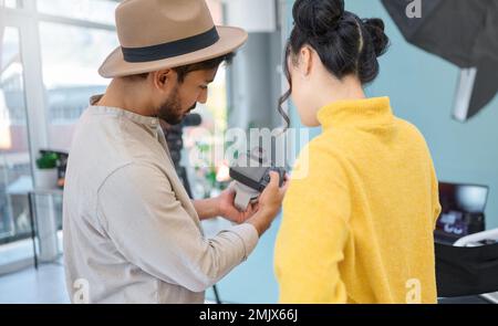 Photography, camera and photographer talking to a model while looking at pictures from a photoshoot. Discussion, studio and young cameraman choosing a Stock Photo