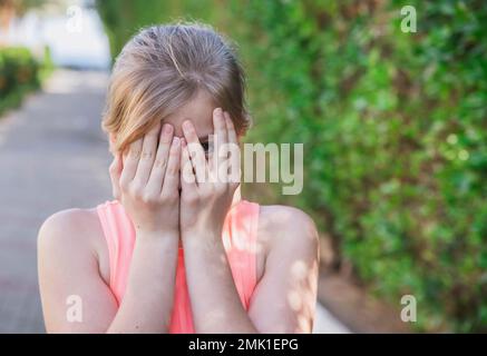 girl hide her face behind hands and peeps with one eye Stock Photo