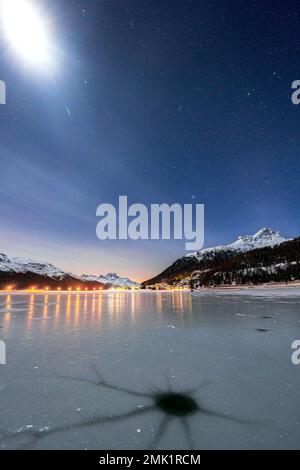 Snowy peak Piz Da La Margna and Silvaplana lit by moon view from the icy lake Champfer, Graubunden canton, Engadine, Switzerland Stock Photo