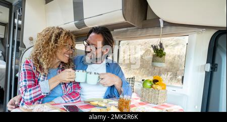 Adult couple toasting inside camper van during travel adventure life vacation. Motor home camper vehicle indoor leisure activity. Concept of traveler Stock Photo