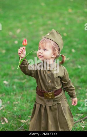 Adorable baby girl in Soviet military uniform with tulip in hands Stock Photo