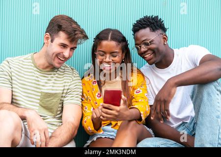 three happy young friends looking mobile phone and smiling with the content - happy teenagers with a smartphone - Lifestyle concept Stock Photo