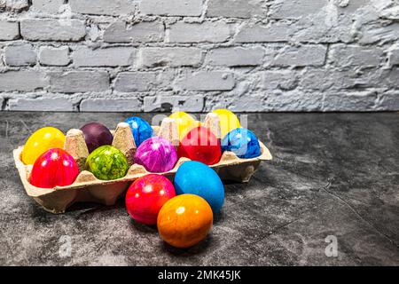 Eggs cardboard with colorful easter eggs in front of white brick wall Stock Photo
