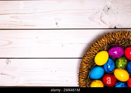 round easter basket with colorful easter eggs on rustic white wooden tabletop Stock Photo