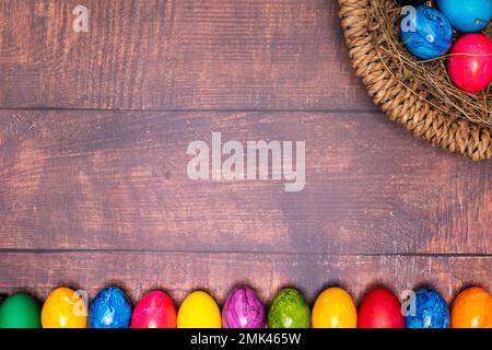 round easter basket with colorful easter eggs on rustic white wooden tabletop Stock Photo