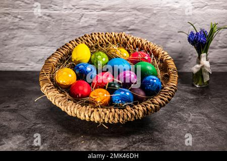 Easter nest with hay and many colorful Easter eggs and a small spring bouquet of flowers Stock Photo