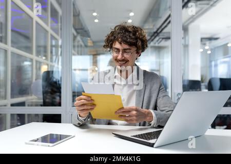 Successful businessman inside office at work, man received notification mail with good news, hispanic man in business suit using laptop at work smiling and reading notification. Stock Photo