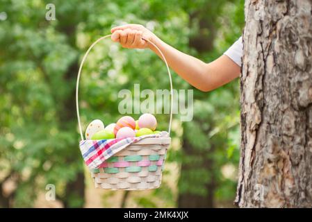Child hand holding basket full of colorful easter eggs after egg hunt Stock Photo