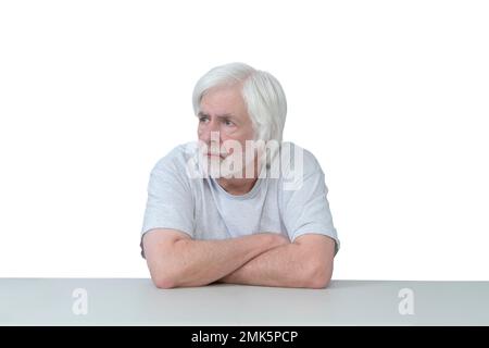 Horizontal shot of an old man sitting at a table with his arms crossed looking away.  Isolated on white.  Lots of copy space. Stock Photo