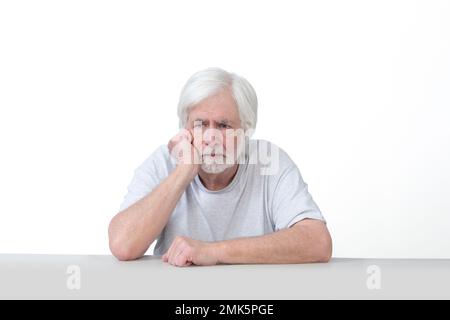 Horizontal shot of an old man sitting at a table with his arms crossed and hand on his jaw in deep thought.  Isolated on white.  Lots of copy space. Stock Photo