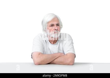 Horizontal shot of an old man sitting at a table with his arms crossed..  Isolated on white.  Lots of copy space. Stock Photo