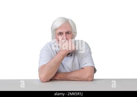 Horizontal shot of an old man sitting at a table with his hand to his chin  deep in deep thought.  Isolated on white.  Lots of copy space. Stock Photo