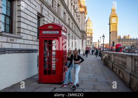 Two Attractive Young Women Pose For A Photo Outside A Traditional British Telephone Box With Big Ben In The Backround, Westminster, London, UK. Stock Photo