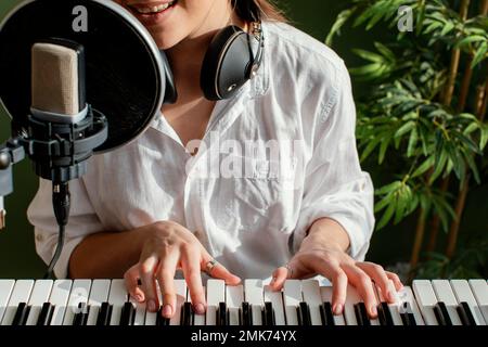 smiley female musician playing piano keyboard indoors singing into microphone. High resolution photo Stock Photo