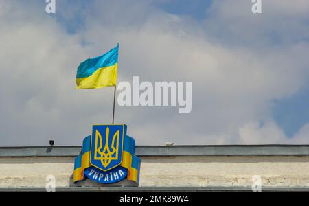 State symbols, flag and coat of arms of Ukraine on sky background. Under the coat of arms the inscription Ukraine, in Ukrainian. Stock Photo