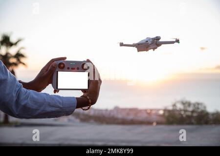 Close up on drone remote control with blank screen for mockup, drone flying beside Stock Photo