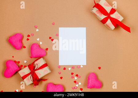 Empty white card, gift boxes and pink hearts on beige background. Concept of Valentine day. Greeting card for Valentine,  Mother day or birthday. Stock Photo