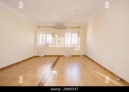 Empty one-story room with two windows with white curtains and light brown tile floors Stock Photo