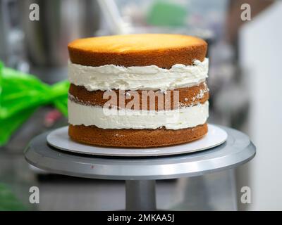 chef pastry designer confectioning a frosted 3 floor layered cake stuffed with strawberries and whipped butter cream. Cake structure before decoration Stock Photo