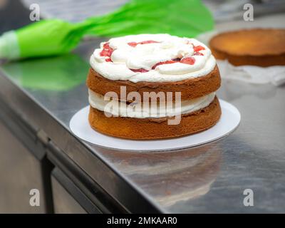 chef pastry designer confectioning a frosted 3 floor layered cake stuffed with strawberries and whipped butter cream. Cake structure before decoration Stock Photo